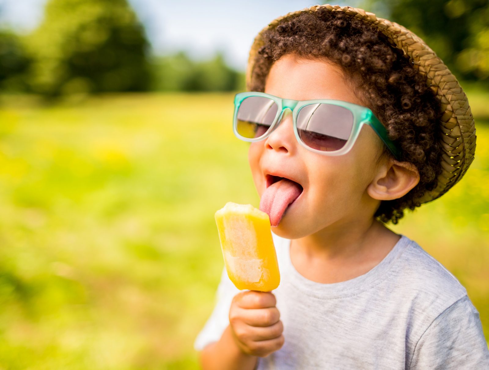 Boy in sunglasses and hat eating ice lolly outdoors