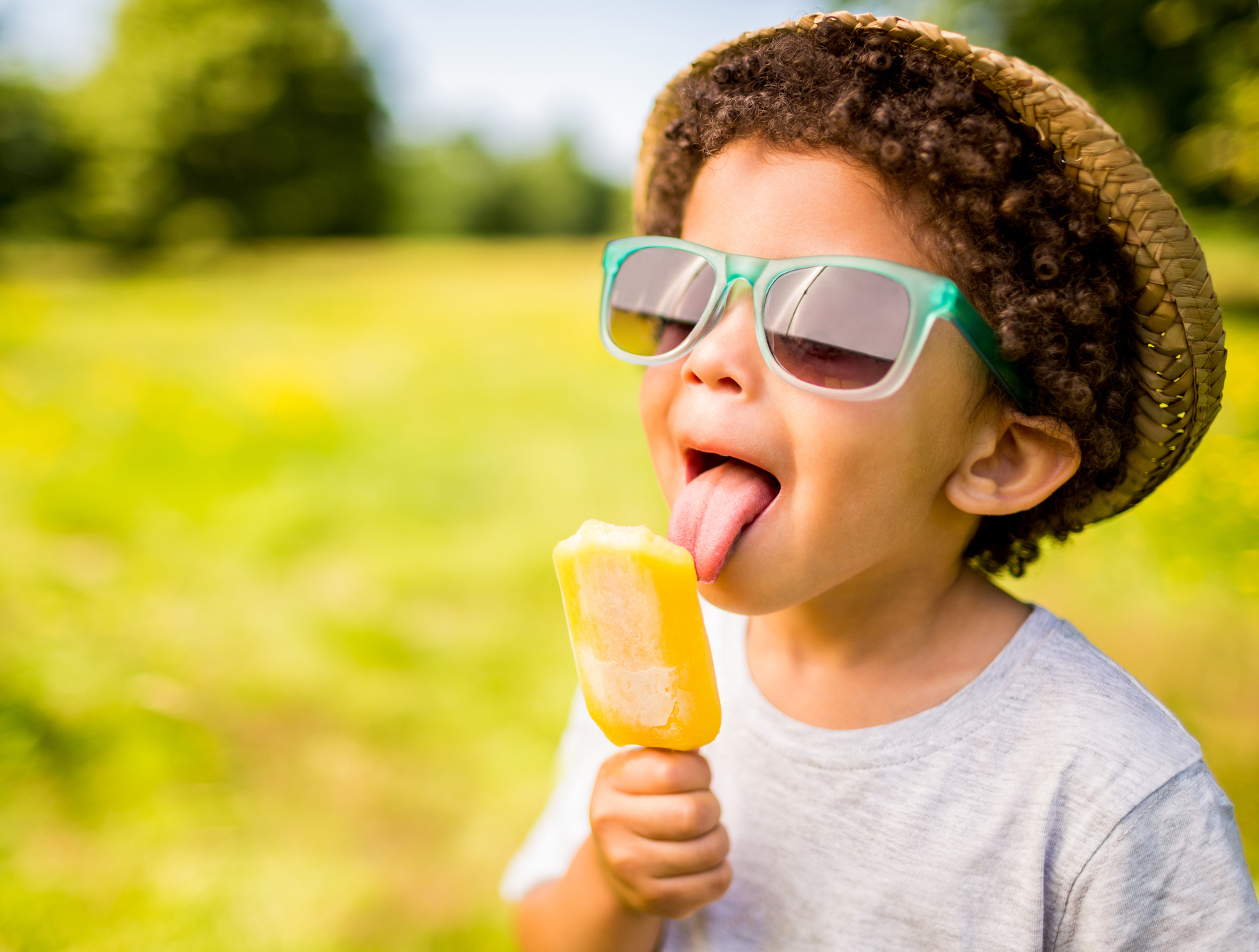 Boy in sunglasses and hat eating ice lolly outdoors